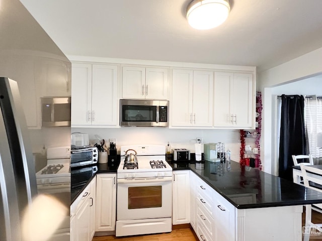 kitchen featuring dark countertops, light wood-type flooring, a peninsula, stainless steel appliances, and white cabinetry