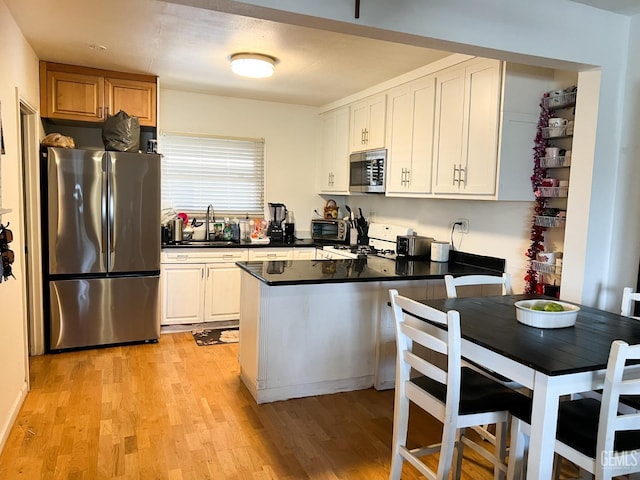 kitchen with dark countertops, light wood finished floors, a peninsula, stainless steel appliances, and a sink