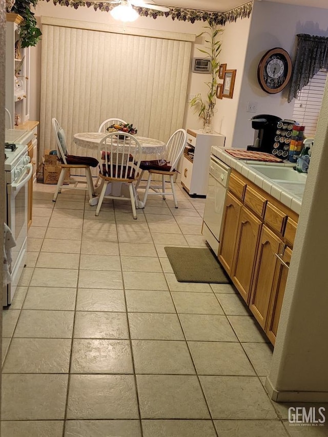 kitchen with tile countertops, light tile patterned floors, brown cabinets, white appliances, and a sink