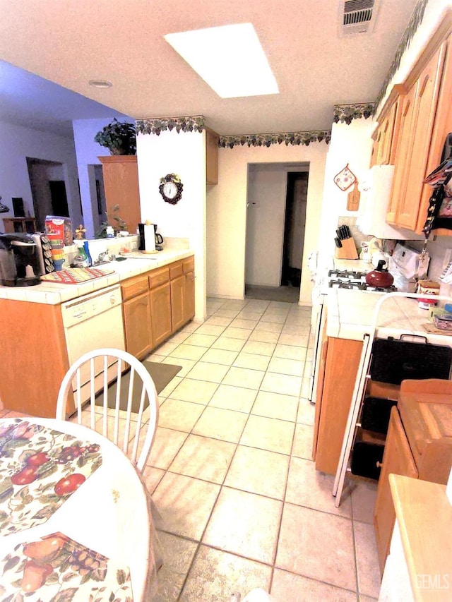 kitchen with light tile patterned floors, visible vents, dishwasher, and tile counters