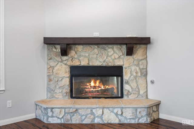 details featuring a stone fireplace, baseboards, and wood finished floors