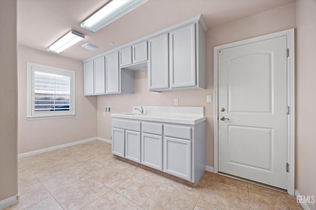 kitchen with tile countertops, light tile patterned floors, a sink, and baseboards