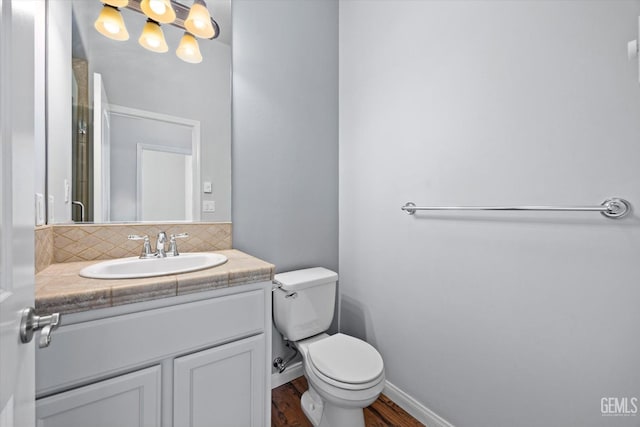 bathroom with toilet, wood finished floors, vanity, baseboards, and backsplash