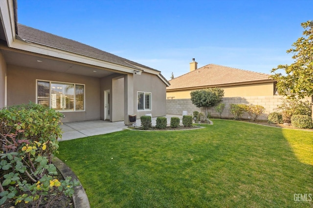 rear view of property featuring a yard, a patio area, fence, and stucco siding