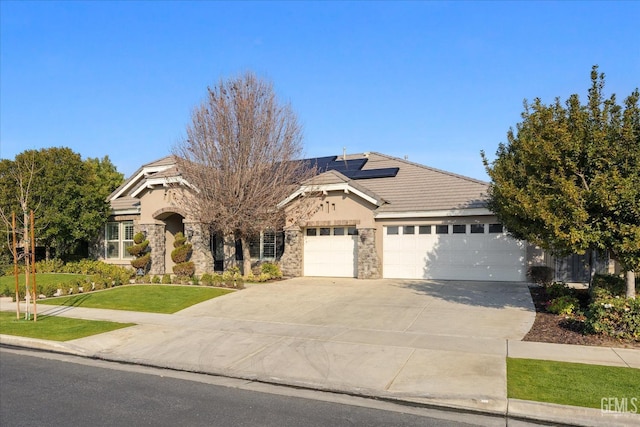 view of front of home with an attached garage, solar panels, stone siding, a tiled roof, and a front yard