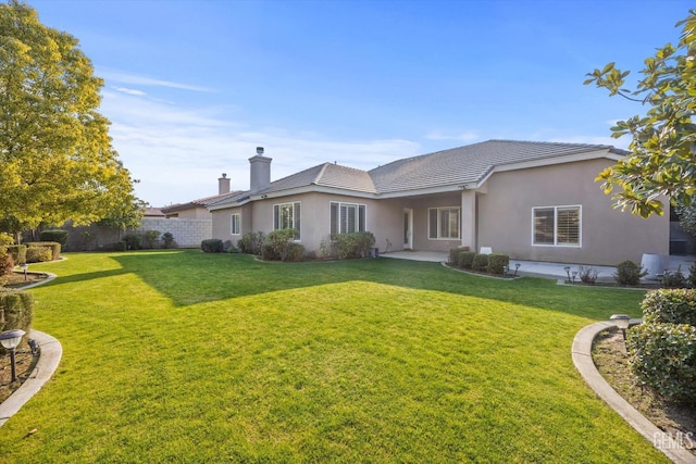 rear view of house with a patio, a lawn, fence, and stucco siding