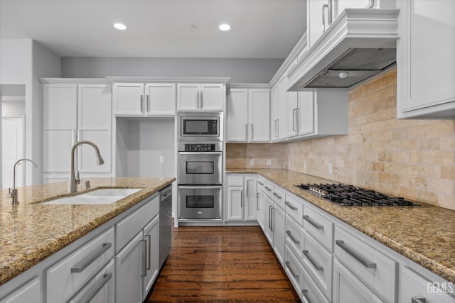 kitchen with stainless steel appliances, premium range hood, a sink, and white cabinetry