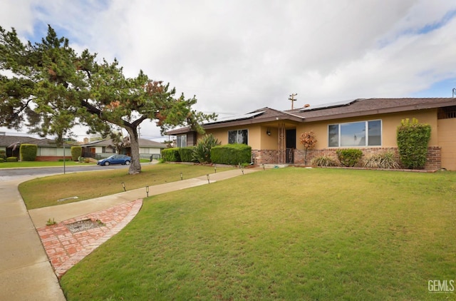 single story home with a front lawn, brick siding, roof mounted solar panels, and stucco siding