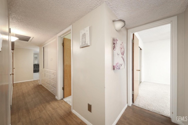 corridor featuring visible vents, a textured ceiling, baseboards, and wood finished floors