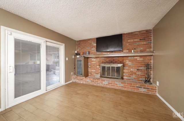 unfurnished living room with baseboards, a textured ceiling, wood finished floors, and a fireplace