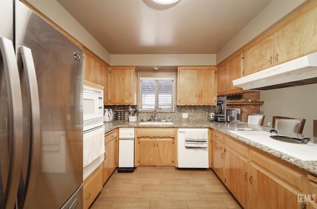 kitchen with a sink, under cabinet range hood, tasteful backsplash, freestanding refrigerator, and white microwave