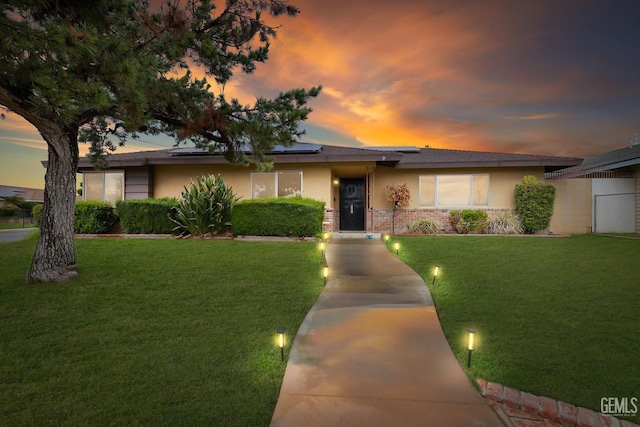 single story home featuring a lawn, brick siding, roof mounted solar panels, and stucco siding