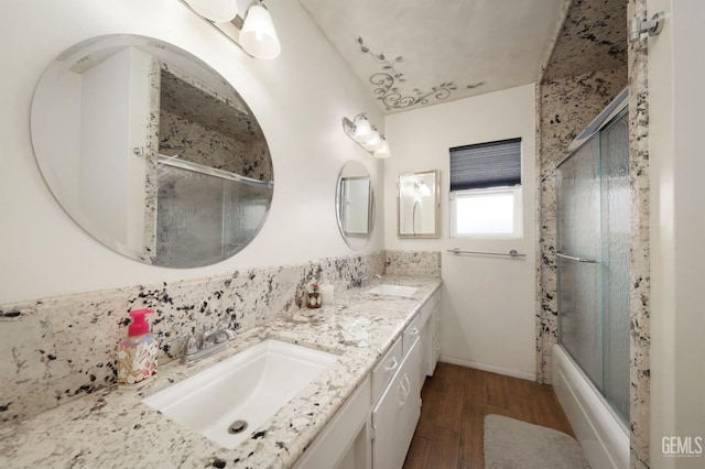 full bathroom featuring double vanity, wood finished floors, bath / shower combo with glass door, and a sink