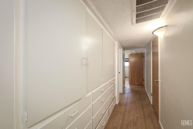 hall featuring visible vents, a textured ceiling, and wood finished floors