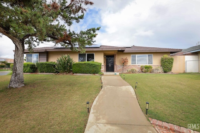 ranch-style house featuring solar panels, a front yard, and stucco siding