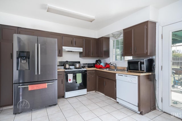 kitchen with stainless steel appliances, sink, light tile patterned floors, and dark brown cabinetry