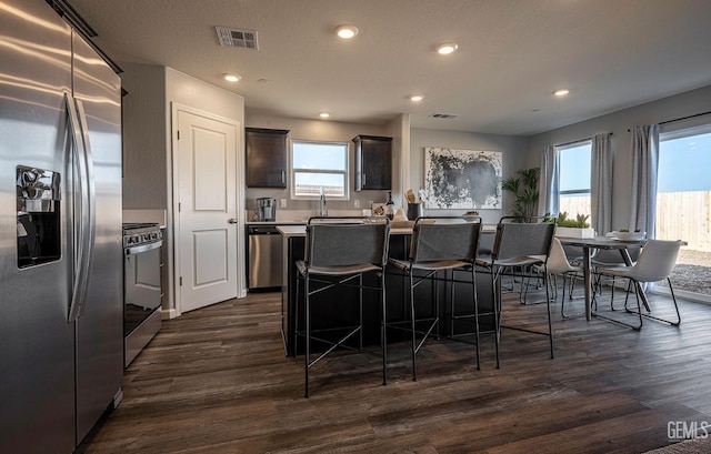 kitchen with dark wood-type flooring, stainless steel appliances, a center island, and dark brown cabinets