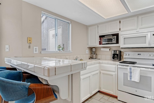 kitchen with white appliances, light tile patterned floors, kitchen peninsula, white cabinets, and tile counters