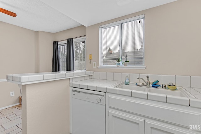 kitchen featuring white dishwasher, tile countertops, sink, white cabinetry, and kitchen peninsula