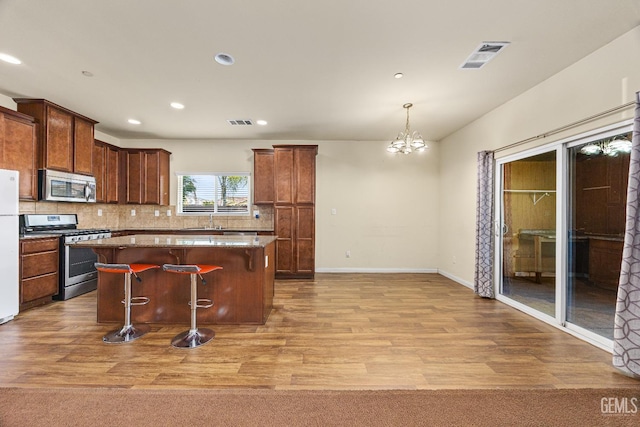 kitchen featuring visible vents, a kitchen island, light wood-style floors, a kitchen breakfast bar, and appliances with stainless steel finishes