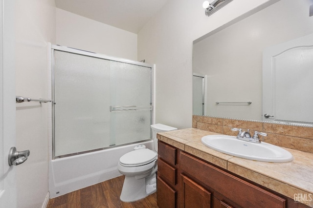 full bath with toilet, enclosed tub / shower combo, wood finished floors, and vanity