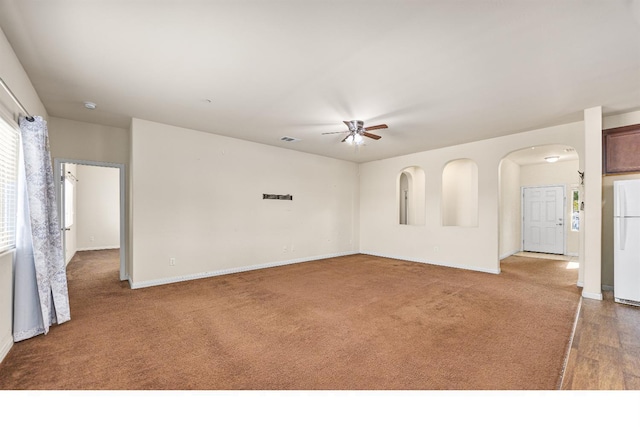 carpeted empty room with arched walkways, ceiling fan, visible vents, and baseboards