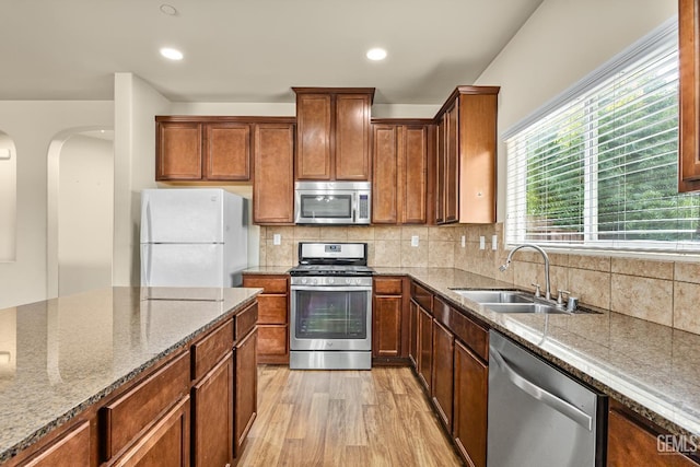 kitchen featuring appliances with stainless steel finishes, arched walkways, a sink, light stone counters, and light wood-style flooring