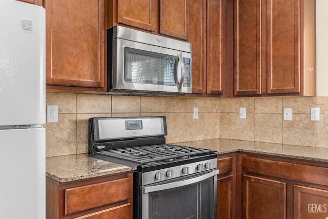 kitchen with backsplash, stainless steel appliances, brown cabinetry, and light stone countertops