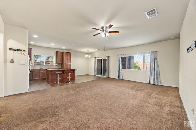 unfurnished living room featuring plenty of natural light, carpet, ceiling fan with notable chandelier, and visible vents