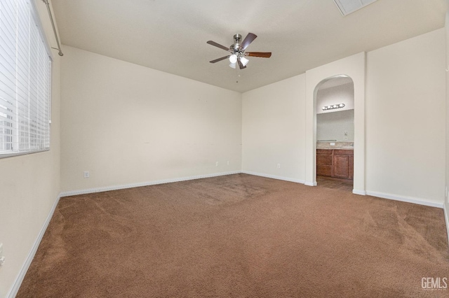 unfurnished bedroom featuring carpet floors, baseboards, arched walkways, and connected bathroom