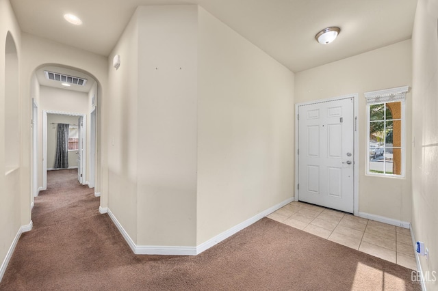 carpeted entryway featuring arched walkways, baseboards, visible vents, and tile patterned flooring