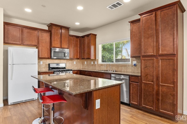 kitchen featuring visible vents, a kitchen island, light wood-type flooring, a sink, and stainless steel appliances