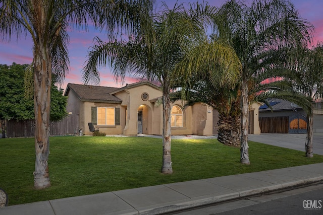 mediterranean / spanish house with fence, driveway, stucco siding, a yard, and a tile roof