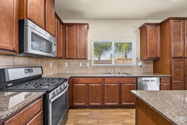 kitchen with stainless steel appliances, stone counters, a sink, and light wood-style floors