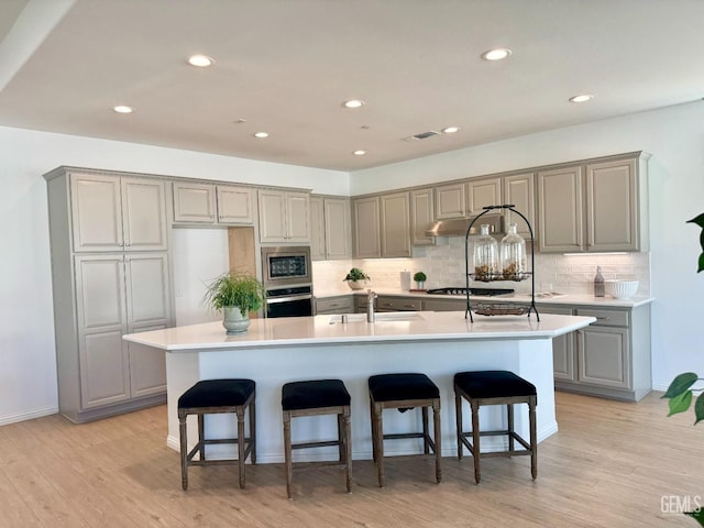 kitchen with stainless steel appliances, a kitchen island with sink, sink, and light hardwood / wood-style floors