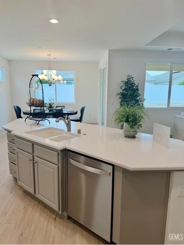 kitchen with sink, a center island with sink, stainless steel dishwasher, pendant lighting, and light hardwood / wood-style floors