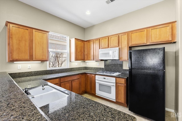 kitchen with sink, white appliances, light tile patterned floors, and dark stone countertops