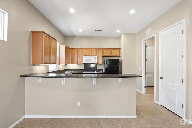 kitchen featuring black refrigerator, dark stone counters, a kitchen breakfast bar, kitchen peninsula, and light tile patterned floors