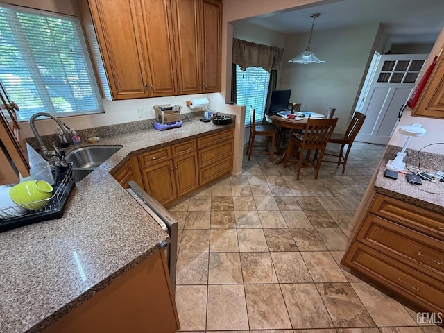 kitchen with a sink, stone counters, brown cabinets, and hanging light fixtures