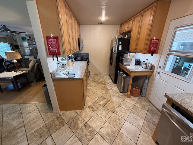 kitchen featuring a ceiling fan, visible vents, appliances with stainless steel finishes, brown cabinets, and open floor plan