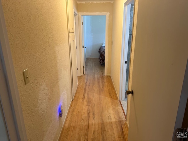 corridor with a textured wall and light wood-style flooring