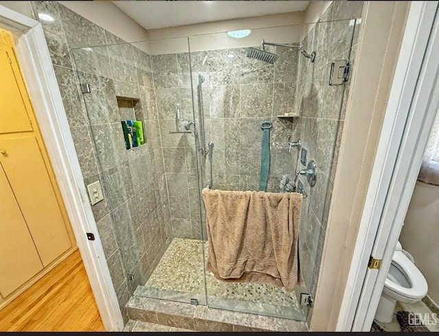 full bath featuring toilet, wood finished floors, and a stall shower