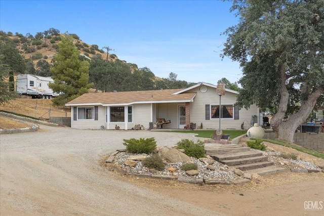 ranch-style house with dirt driveway and fence