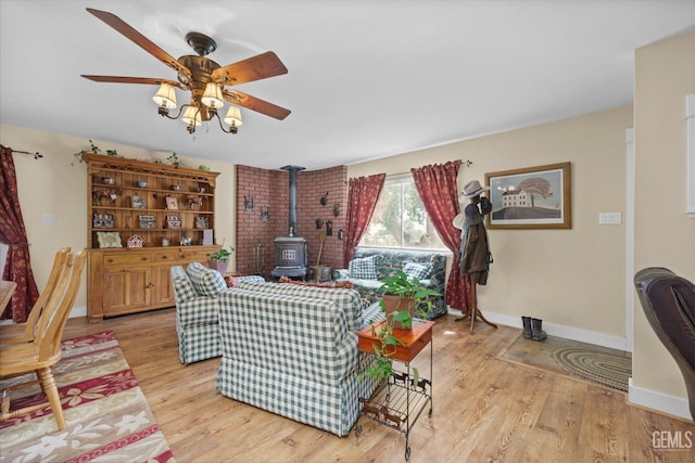 living area with a wood stove, ceiling fan, light wood-style flooring, and baseboards