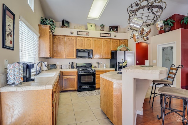 10126 Pyramid Peak Dr, Bakersfield, CA 93311 - kitchen featuring black appliances, a kitchen island, a kitchen bar, a towering ceiling, and tile countertops