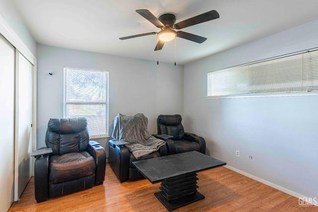 living area with a ceiling fan, light wood-type flooring, and baseboards