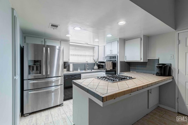 kitchen featuring backsplash, a peninsula, white cabinets, stainless steel appliances, and a sink