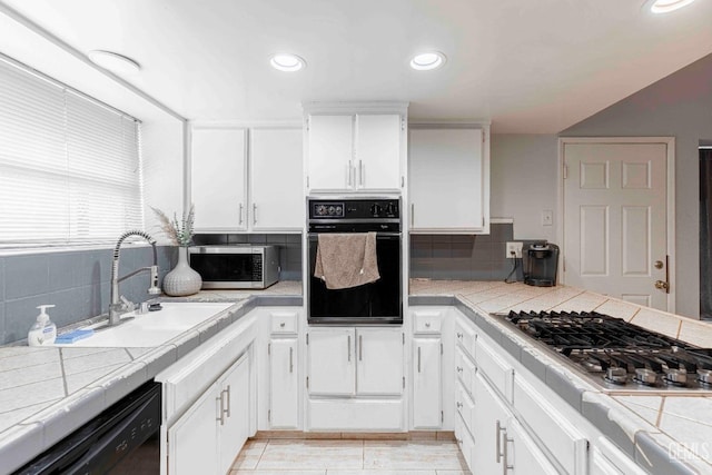 kitchen with white cabinetry, black appliances, tile countertops, and a sink