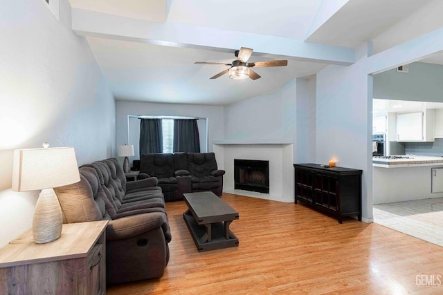 living area featuring beamed ceiling, visible vents, light wood-style flooring, a ceiling fan, and a brick fireplace