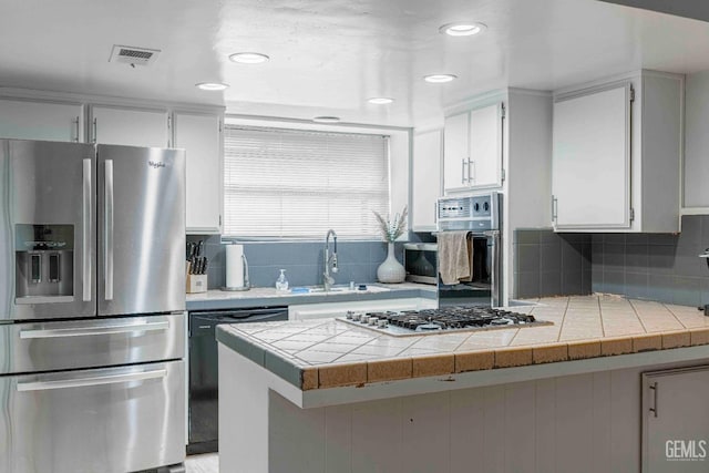 kitchen with stainless steel appliances, visible vents, tile counters, and white cabinets